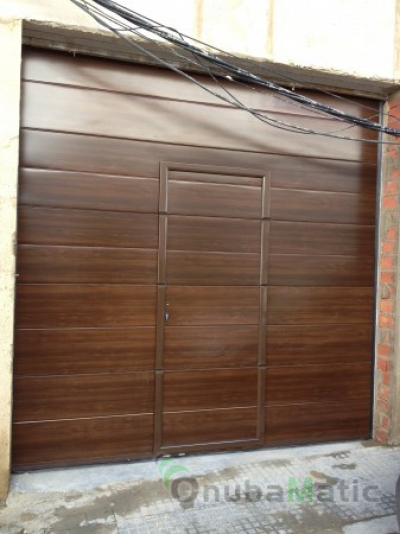 Puerta seccional automática imitación madera con puerta peatonal en vivienda unifamiliar en Trigueros
