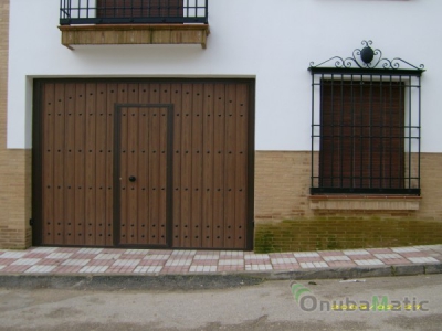 Puerta automática no desbordante en madera Werzalit con adornos de clavos y puerta peatonal en vivienda unifamiliar en Almonte.