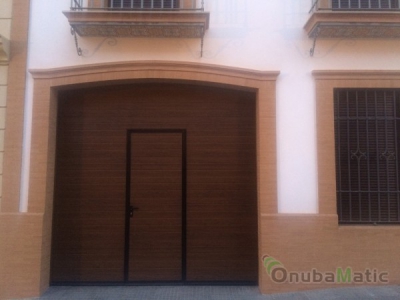Puerta seccional automática imitación madera con puerta peatonal en vivienda unifamiliar en Gibraleón.